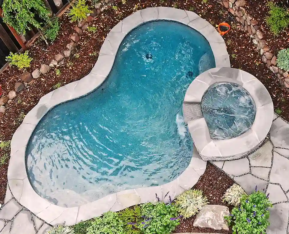 Aerial view of a kidney-shaped swimming pool with hot tub, surrounded by white decking and landscaping.